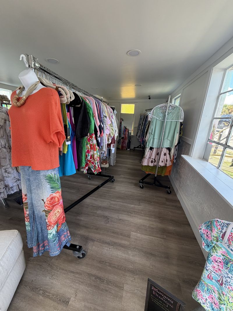 Inside the shop: a coral top and a floral skirt on a form, with racks of colorful clothes and a bright window
